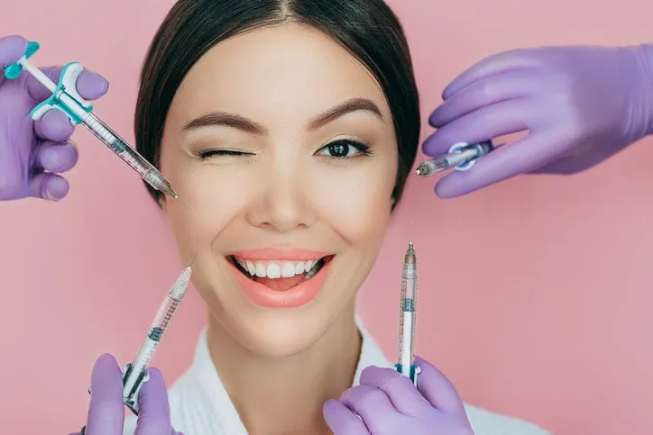 portrait of a beautiful winking woman and many syringes with beauty injections around her face