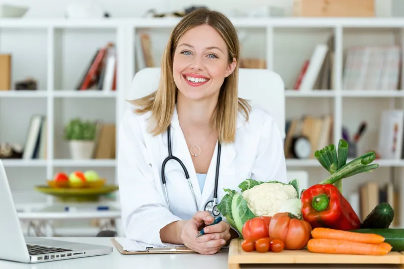 portrait of beautiful smiling nutritionist looking at camera and showing healthy vegetables in the consultation