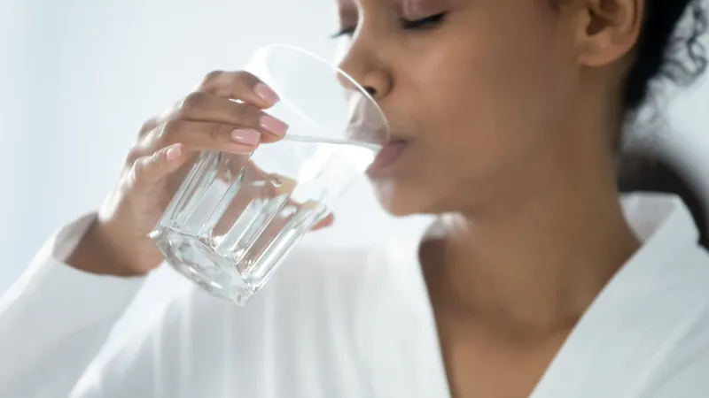 close up beautiful african woman holding glass drinking a pill with still water minerals and vitamins for female, dietary supplement, reducing of thirst, body water balance healthy lifestyle concept