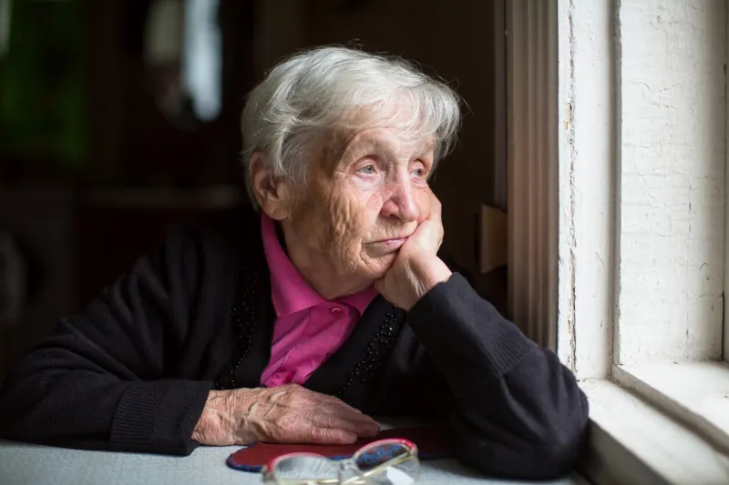 an elderly woman sadly looking out the window melancholy and depressed