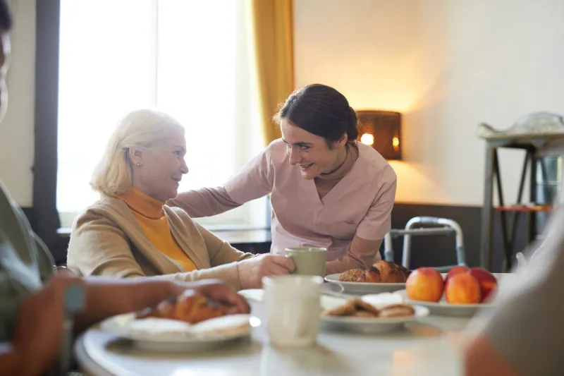 portrait of smiling young woman caring for senior patient in nursing home, copy space