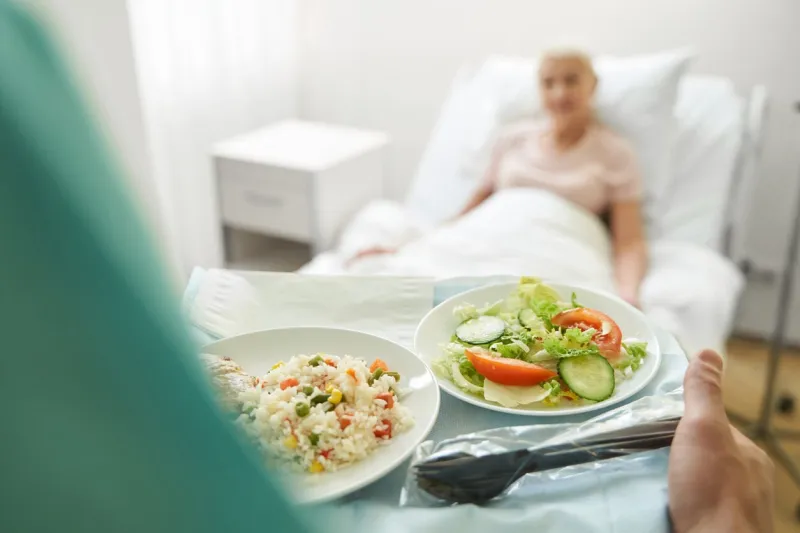 person carrying tray with rice and vegetable salad to patient in bed of heath care center