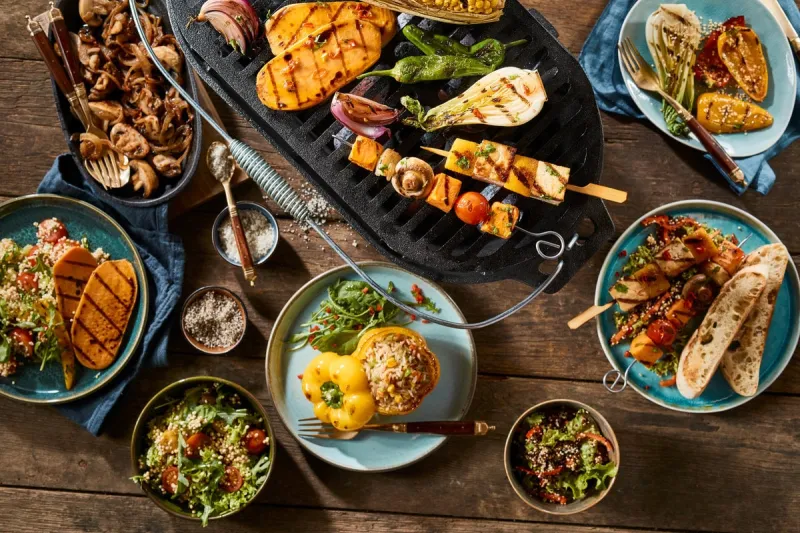 a vegetarian barbecue grill and various gourmet dishes on a rustic timber table