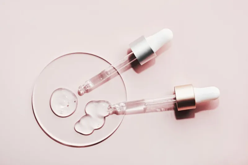 pipettes with different samples of gels cosmetic products in petri dish on pink background