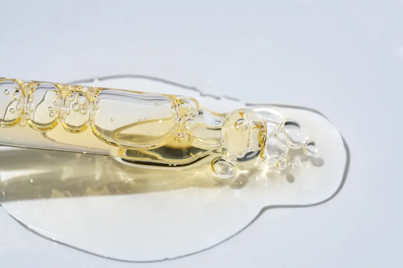 bottle pipette dropper close up and liquid yellow-orange retinol or vitamin c gel or serum on a blue background