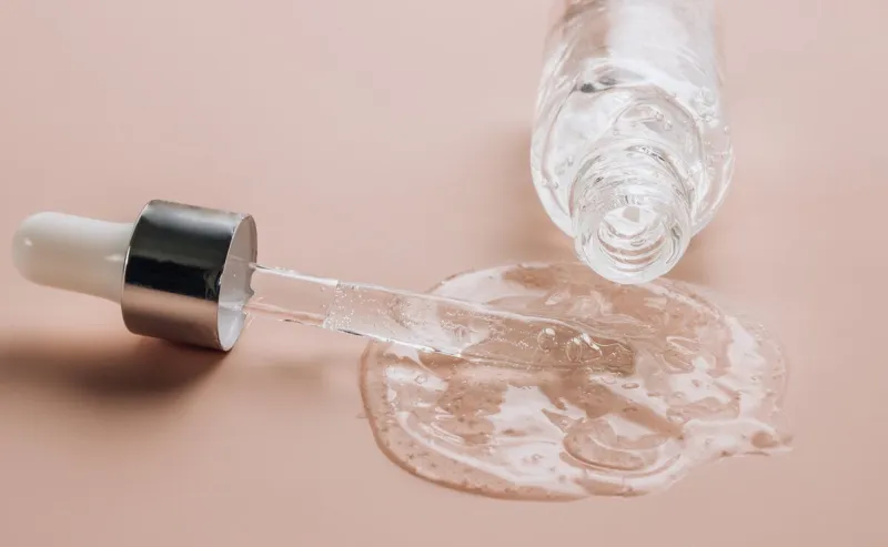 bottle of hyaluronic acid on skin color background with oxygen bubbles selective focus