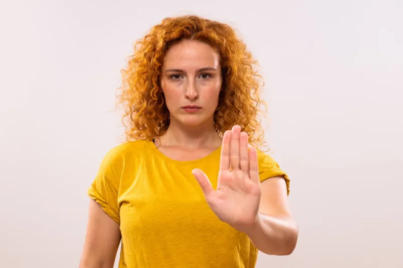 image of serious ginger woman showing stop sign on gray background