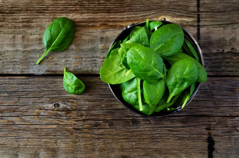 spinach in the bowl on the dark wood background toning selective focus on the lower right leaf