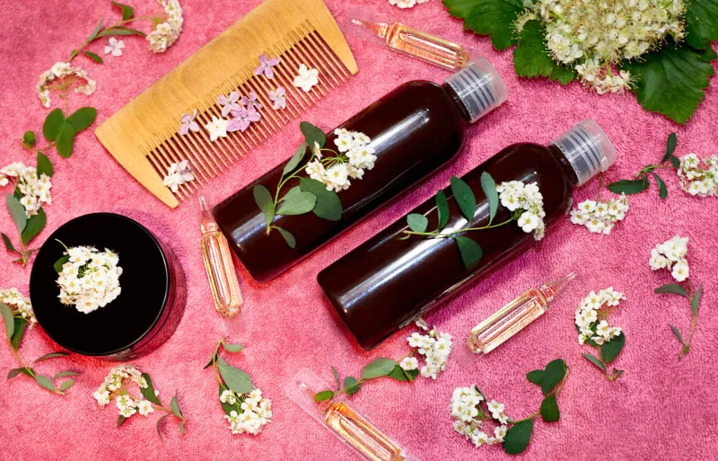 vials with hair care product in fresh flowers on a pink towel
