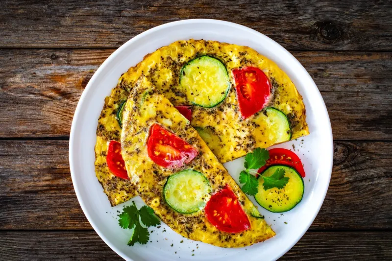 omelette - scrambled eggs with cheese, zucchini and tomatoes on wooden background