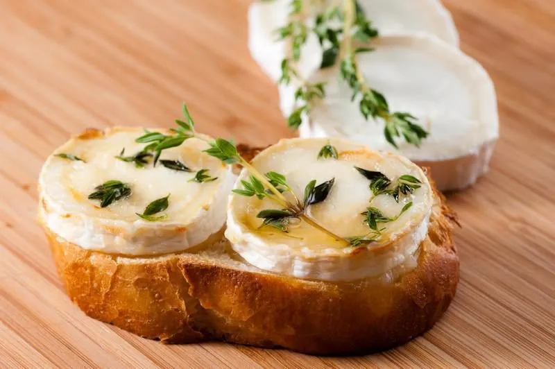 fromage de chèvre sur une tranche de pain gratinée au miel et assaisonnée de thym sur une planche de bambou