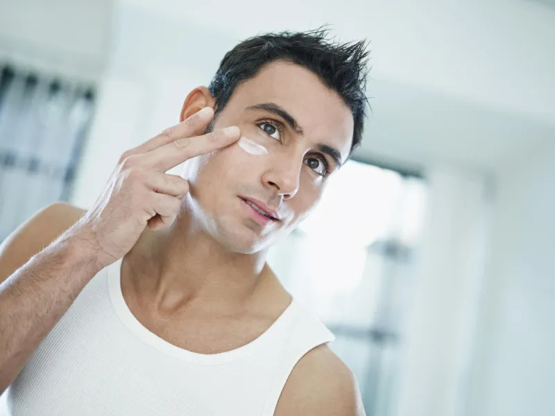 jeune homme caucasien, appliquer la crème pour les yeux sur le visage de forme horizontale, vue de face, la tête et les épaules