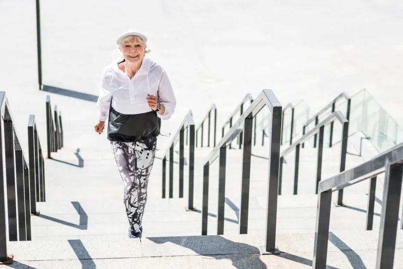 portrait of happy old woman raising upstairs she is jogging on city ladder construction and smiling