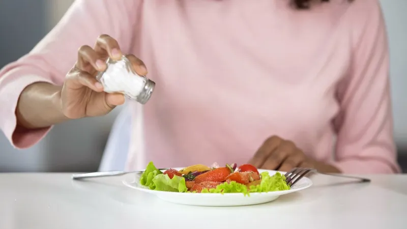 woman adding too much salt to her food, unhealthy eating, dehydration problems