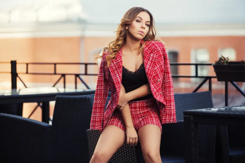 young fashion woman sitting on chair at sidewalk cafe stylish female model in red tweed jacket and shorts suit