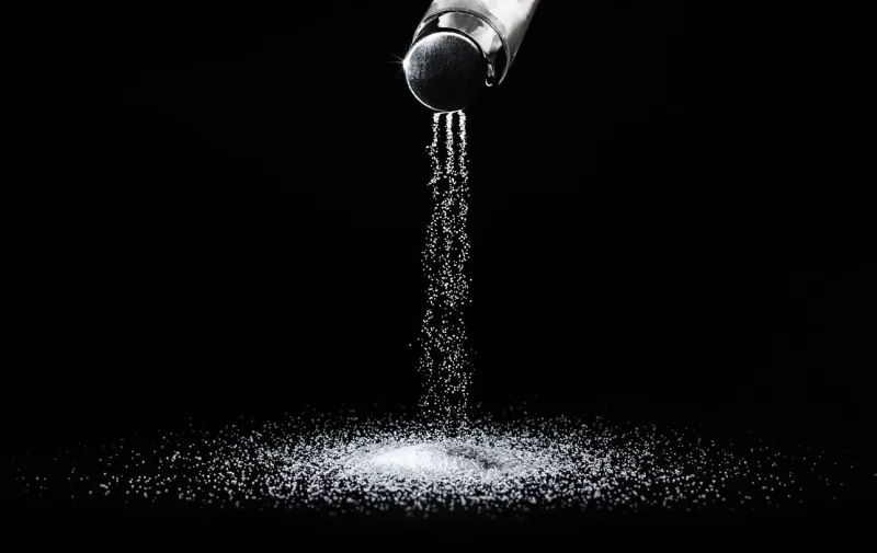 salt spills out of the salt shaker in thin streams on a black backgroundconcept salting