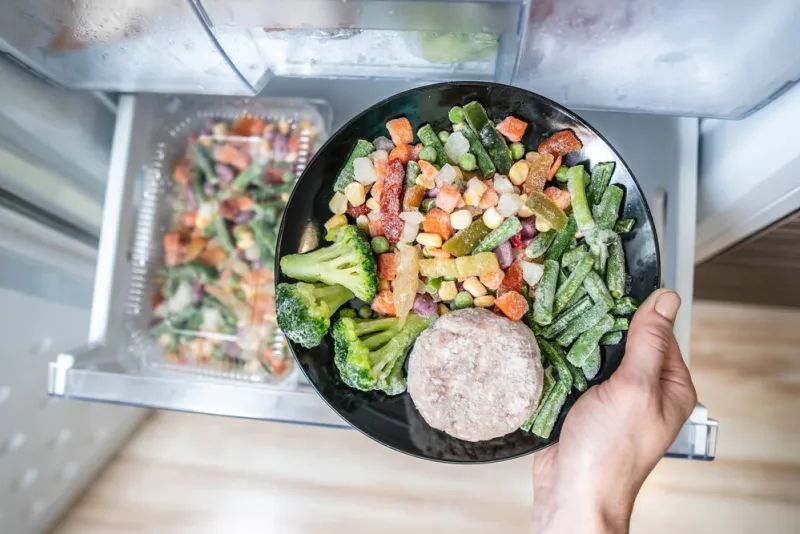 hands are taking a plate of frozen food out of the freezer of the fridge concept of storing ready made food and saving time on cooking dinner
