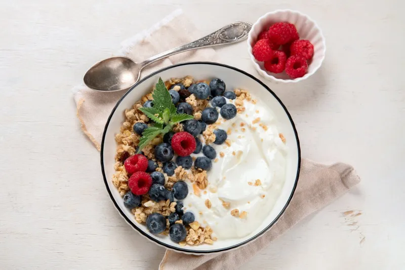 granola with yogurt and berries for healthy breakfast bowl of greek yogurt with granola, blueberries and raspberries on a white background, top view