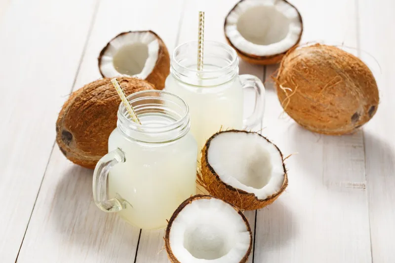refreshing coconut water in jars and coconuts on a wooden white background