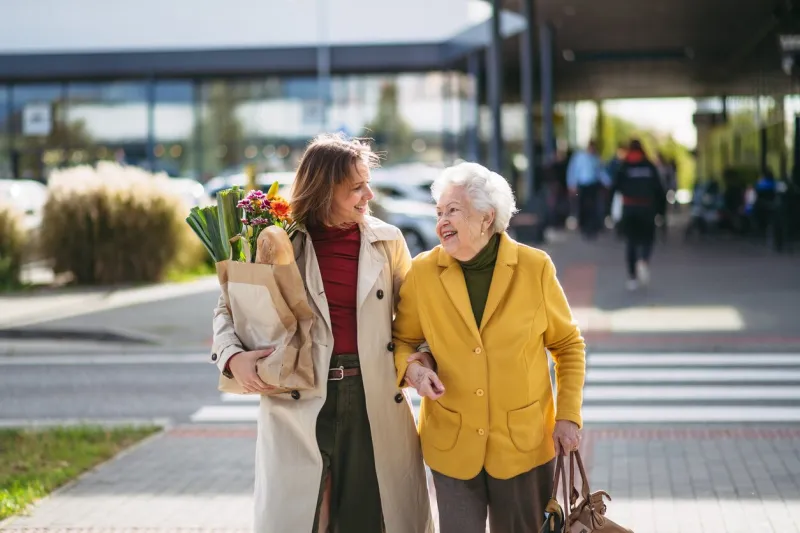 mature granddaughter carrying groceries out to her grandmother's car senior woman shopping at the shopping center, needing help loading groceries into the car