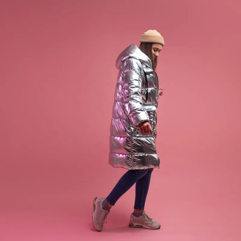 trendy autumn and winter clothing, studio shot on a pink background, copy space a cool girl in a shiny silver down jacket and a knitted hat
