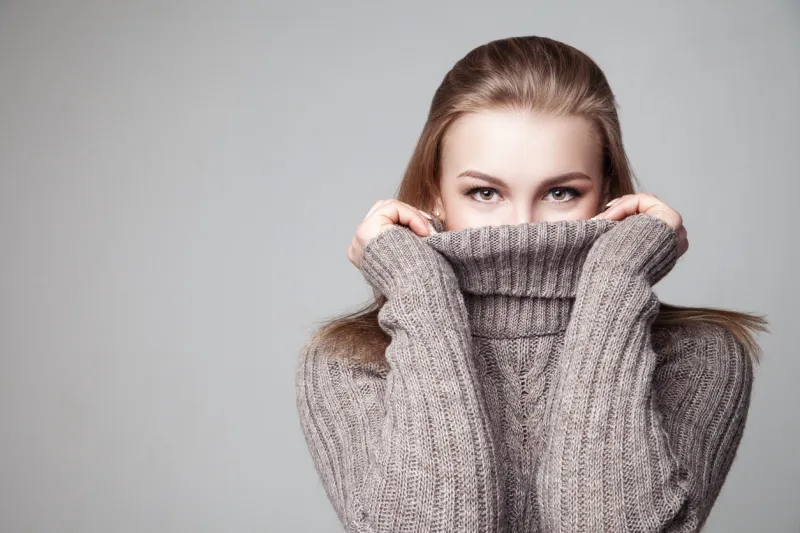 beautiful blond young girl wears winter pullover over gray background