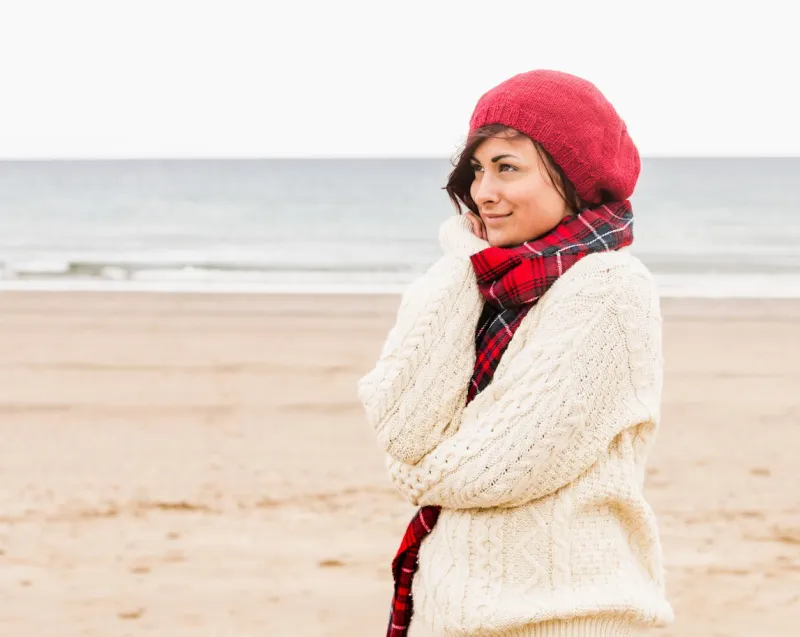 side view of a cute young woman in stylish warm clothing looking away on the beach