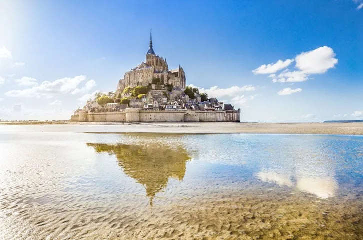 panoramic view of famous le mont saint-michel tidal island on a sunny day with blue sky and clouds, normandy, northern france