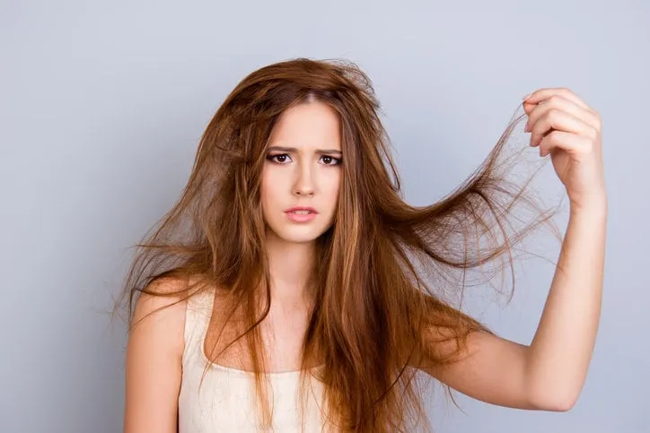 close up portrait of frustrated young girl with messed hair on pure background, wearing white casual singlet, holding her hair