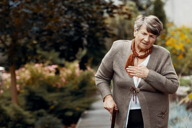 weak senior woman with walking stick waiting for help during breathlessness attack