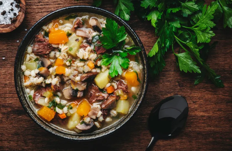 autumn food warming soup with pumpkin, mushrooms, vegetables, beef and barley rustic wood table background, top view
