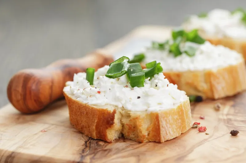crunchy baguette slices with cream cheese and green onion on olive board, shallow focus