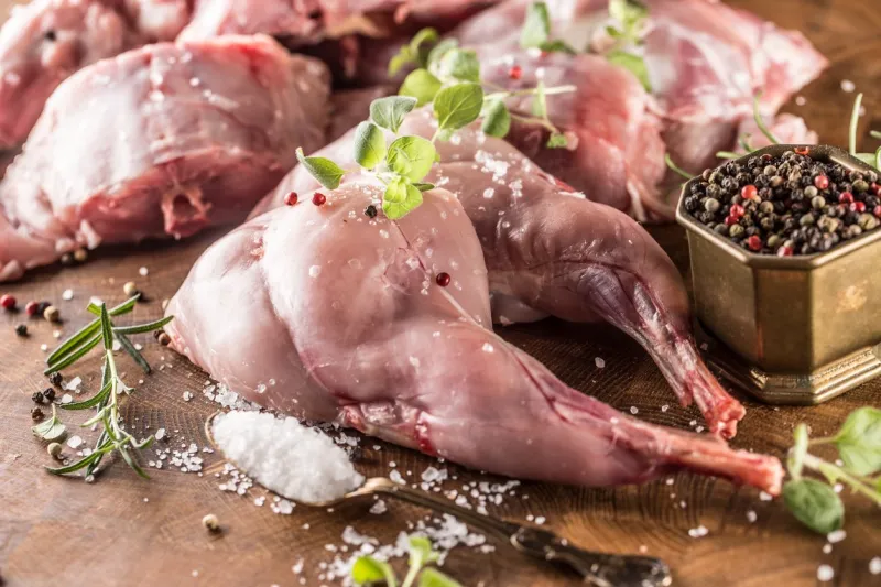 portioned rabbit legs and saddle with herbs and spices on butcher board