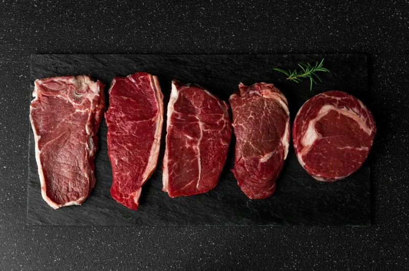 selection of raw beef meat food steaks against black stone background new york striploin steak, top blade, rib eye, and other cuts of meat