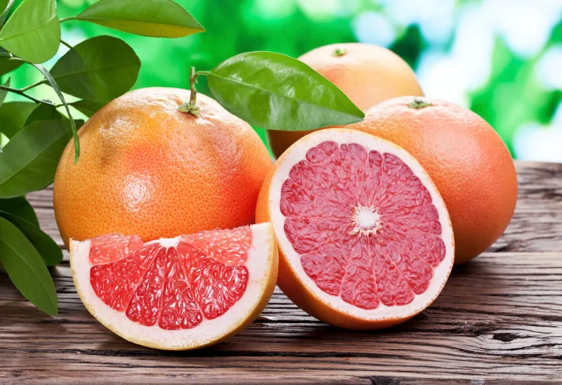 grapefruits on a wooden table with green foliage on the background