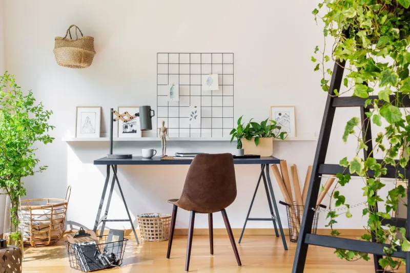 brown chair at desk in white boho home office interior with plants and posters real photo