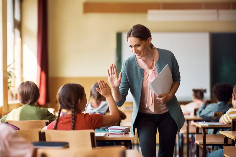 happy elementary school teacher giving high-five to her student during class in the classroom
