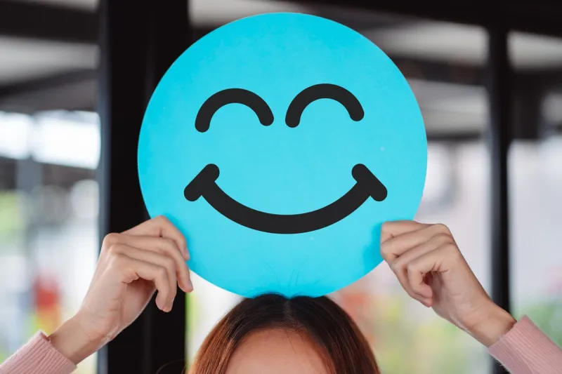 asian woman holding blue happy smile face on paper cut, user giving good feedback rating, think positive , customer review, assessment, of mental health day, compliment day, satisfaction concept