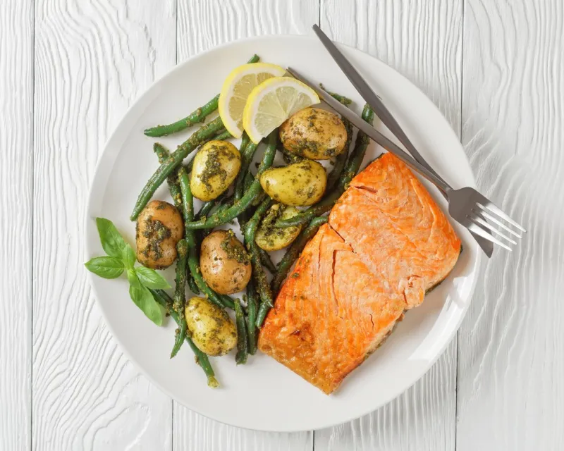 roast salmon fillet with pesto dressed green beans and new potatoes on a white plate on a white wooden table, flat lay