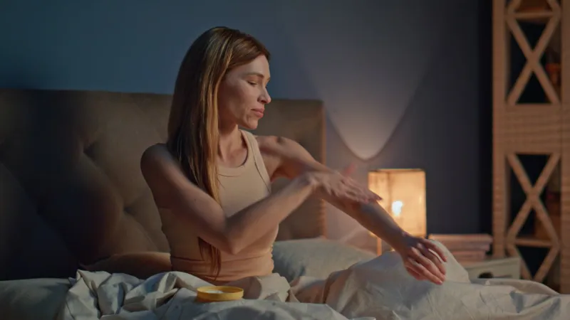woman applying cream to arms preparing to sleep in comfortable bed smiling beautiful girl moisturizing hands skin with body lotion at evening carefree lady enjoy skincare routine with cosmetics