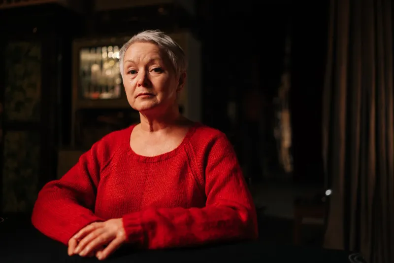 low-angle view portrait of grey-haired mature adult woman receiving forecasting future during divination session sitting at table in dark room, by light of burning candle, looking at camera