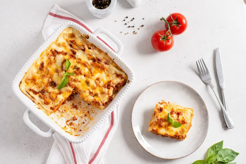 tasty lasagna with meat and cheese on a plate, top view traditional italian lasagna with vegetables, basil, minced beef meat, tomato and cheese on white concrete background restaurant menu, recipe