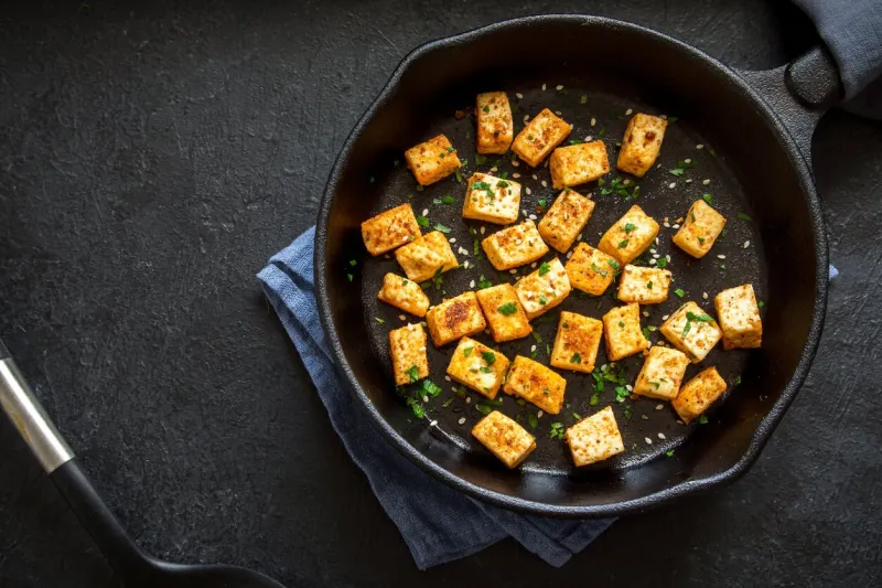 fried tofu with sesame seeds and spices on cast iron pan, copy space healthy ingredient for cooking vegan vegetarian diet food roasted tofu over black background