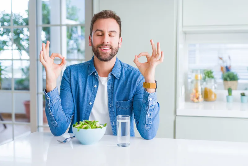 handsome man eating fresh healthy salad relax and smiling with eyes closed doing meditation gesture with fingers yoga concept