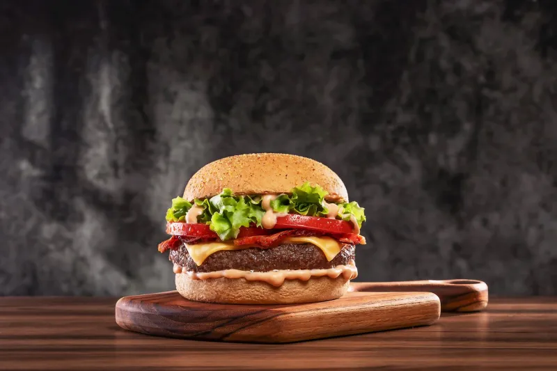 cheeseburger with tomato and lettuce on wooden board