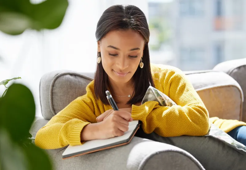 shot of a young woman writing in a diary at home