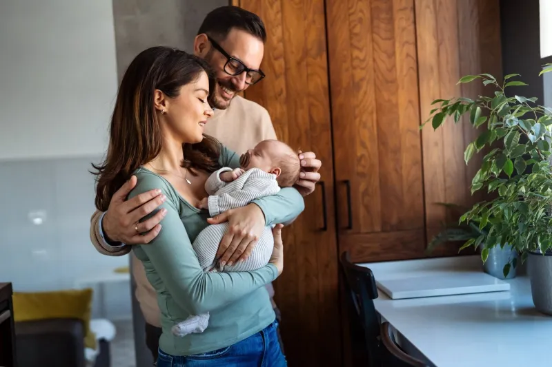 portrait of young happy man and woman holding newborn cute babe dressed in white unisex clothing caucasian smiling father and mother embracing tenderly adorable new born child happy family concept