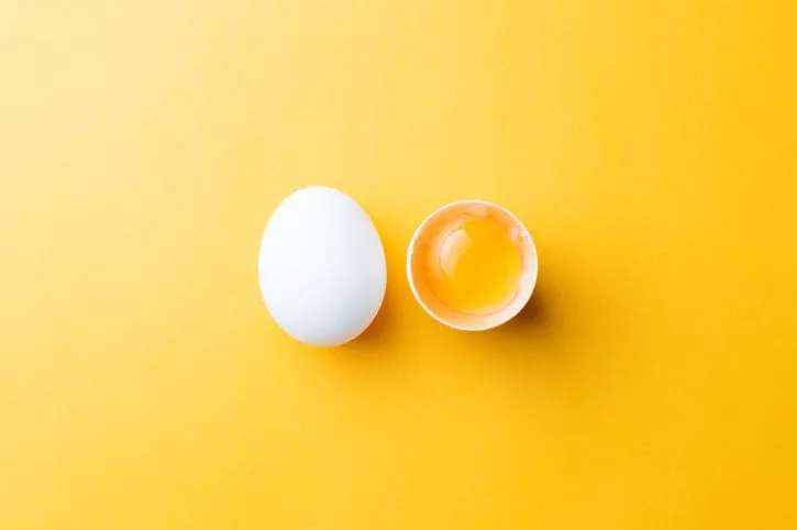 white egg and egg yolk on the yellow background topview