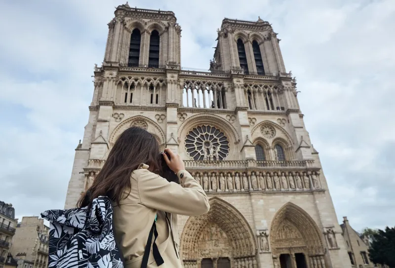 young stylish woman tourist photographing with old camera standing in front of the famous notre dame cathedral in paris