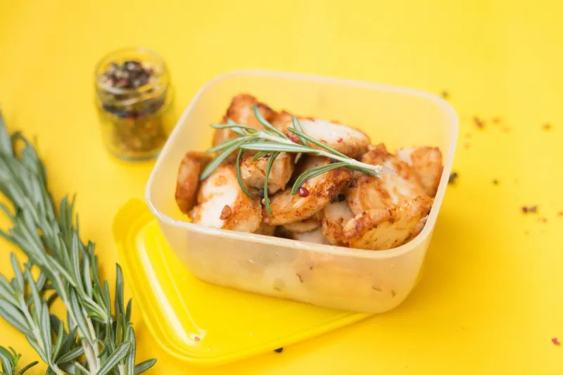 top view of bucket with roasted spicy chicken and sprig of rosemary container for food on a bright yellow background